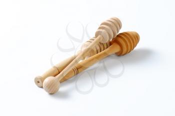 three wooden honey dippers on off-white background