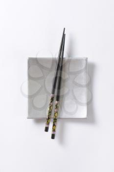 A pair of black chopsticks on empty square silver sushi plate
