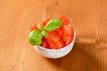 Bowl of halved red plum tomatoes on wooden table