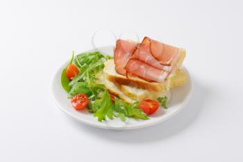 slices of white bread with schwarzwald ham, salad greens and halved cherry tomatoes on white plate