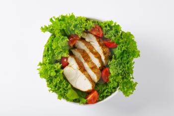 Slices of spice-rubbed chicken breast fillet on bed of lettuce and cherry tomatoes