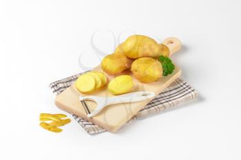 fresh potatoes and peeler on wooden cutting board