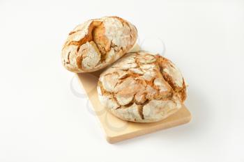 two fresh whole bread cobs on wooden cutting board