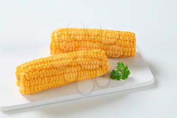 two boiled corn cobs on white cutting board