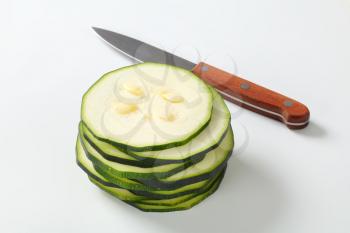 stack of thin slices of fresh zucchini with a sharp knife on a white background