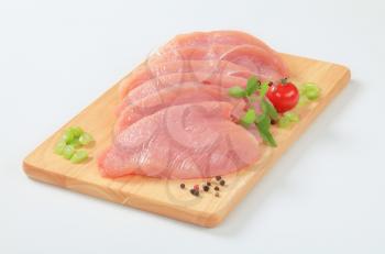 Raw turkey breast escalopes on cutting board
