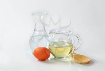 carafe of cold water, jug of sunflower oil, egg and wooden spoon