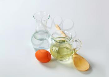 carafe of cold water, jug of sunflower oil, egg and wooden spoon