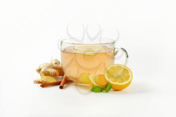 cup of ginger tea with lemon, fresh ginger root and cinnamon sticks on white background