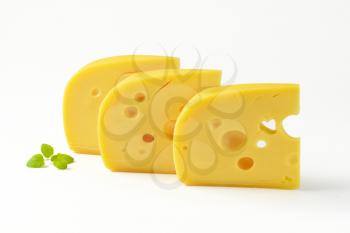 three wedges of yellow medium-hard cheese with eyes on white background