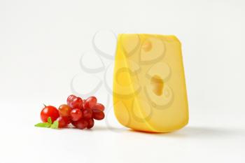 wedge of yellow medium-hard cheese with eyes and fresh red grapes