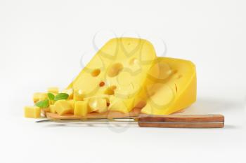 Wedges and cubes of Swiss cheese on wooden cutting board, cheese knife next to it