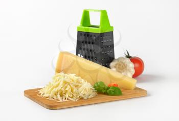 grater and heap of grated parmesan cheese on wooden cutting board