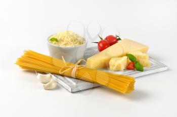 parmesan cheese, vegetables and bundle of raw spaghetti on wooden cutting board