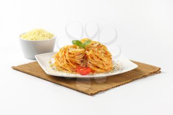 plate of cooked spaghetti with red pesto and grated parmesan cheese on brown place mat