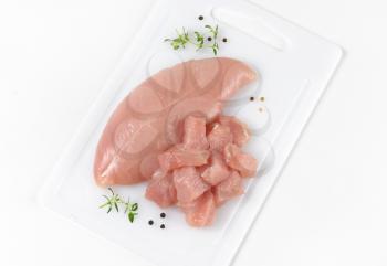 raw turkey breast fillet - whole and diced - on white plastic cutting board