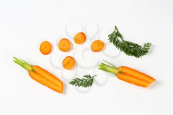 sliced fresh carrots with leaves on white background