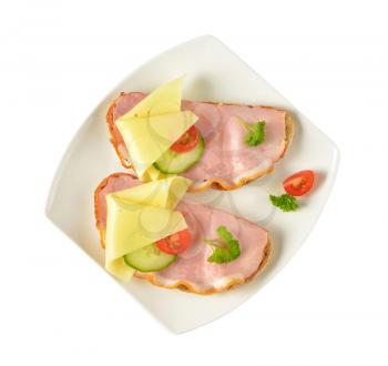 two open faced sandwiches with ham and cheese on white plate