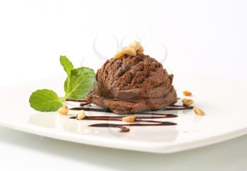 scoop of chocolate ice cream with mint and chopped nuts on white square plate