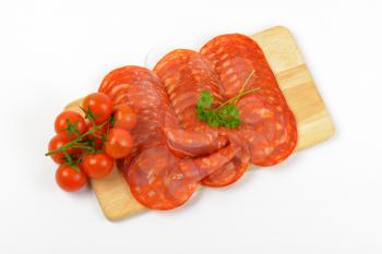 slices of chorizo salami and cherry tomatoes on wooden cutting board