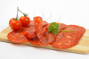 slices of chorizo salami and cherry tomatoes on wooden cutting board - close up