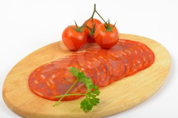 slices of chorizo salami and cherry tomatoes on oval wooden cutting board - close up