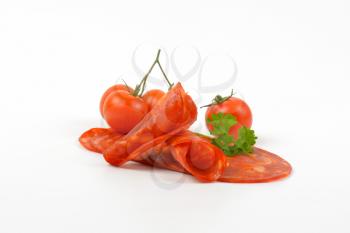 slices of chorizo salami with parsley and cherry tomatoes on white background