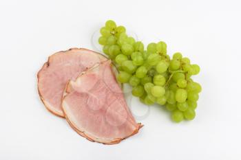 slices of ham and bunch of white grapes on white background