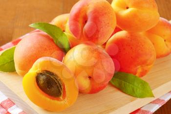 pile of ripe apricots with leaves on wooden cutting board