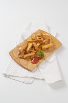 heap of fried chipped potatoes with ketchup on wooden cutting board