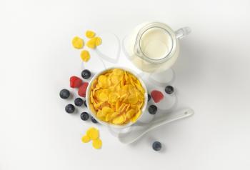 bowl of corn flakes and jug of milk on white background