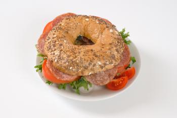 bagel sandwich with salami on white plate