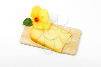 slice of gouda cheese with hibiscus flower on wooden cutting board