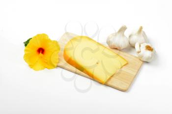 slice of gouda cheese with garlic and hibiscus flower on wooden cutting board