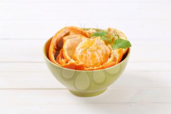 peeled tangerine arranged in peels in green bowl