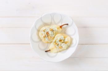 bowl of halved pears with blue cheese and walnuts on white background