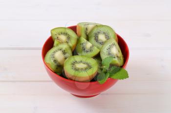 fresh kiwi fruits cut into halves and quarters in red bowl