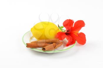 ripe lemon, red hibiscus bloom and cinnamon sticks on white plate