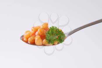 spoon of beans in tomato on white background