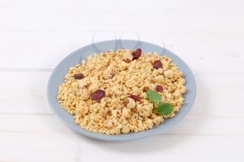 plate of granola with hazelnuts and dried cranberries on white wooden background