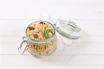 jar of granola with hazelnuts and raisins on white wooden background