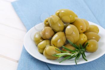 plate of green olives with fresh rosemary on blue place mat - close up