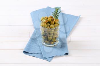 glass of green olives stuffed with red pepper on blue place mat