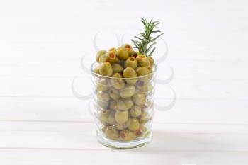 glass of green olives stuffed with red pepper on white background