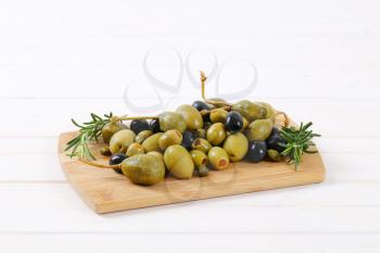 pile of pickled olives, capers and caper berries on wooden cutting board