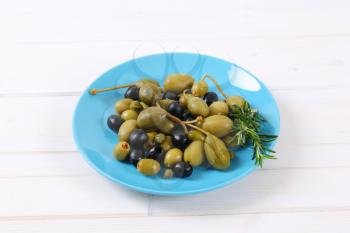 plate of pickled olives, capers and caper berries on white wooden background