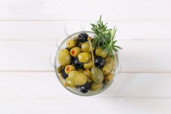 glass of pickled olives, capers and caper berries on white wooden background
