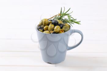 cup of pickled olives, capers and caper berries on white wooden background