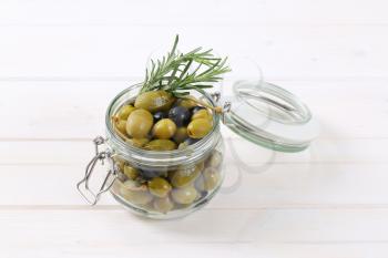 jar of pickled olives, capers and caper berries on white wooden background