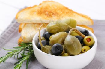 bowl of pickled olives, capers and caper berries with toast